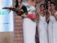Concurso de belleza: ganadora en vestido blanco con corona y ramo de flores, celebrando con aplausos detrás.
