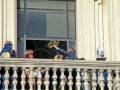 Un hombre con una corona en la cabeza salta del balcón de un edificio, mientras otros observan desde afuera. La imagen parece ser una escena festiva o ceremonial, posiblemente durante un evento importante.