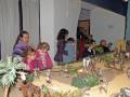 Niños y adultos observan una escena de pesebre en un museo, con figuras de animales y personas en miniatura.