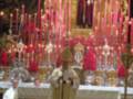 Imagen de un altar con velas rojas, sacerdotes vestidos y una cruz en el fondo.