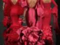 Desfile de moda con modelos en vestidos flamencos rojos con volantes y detalles florales en la cabeza.