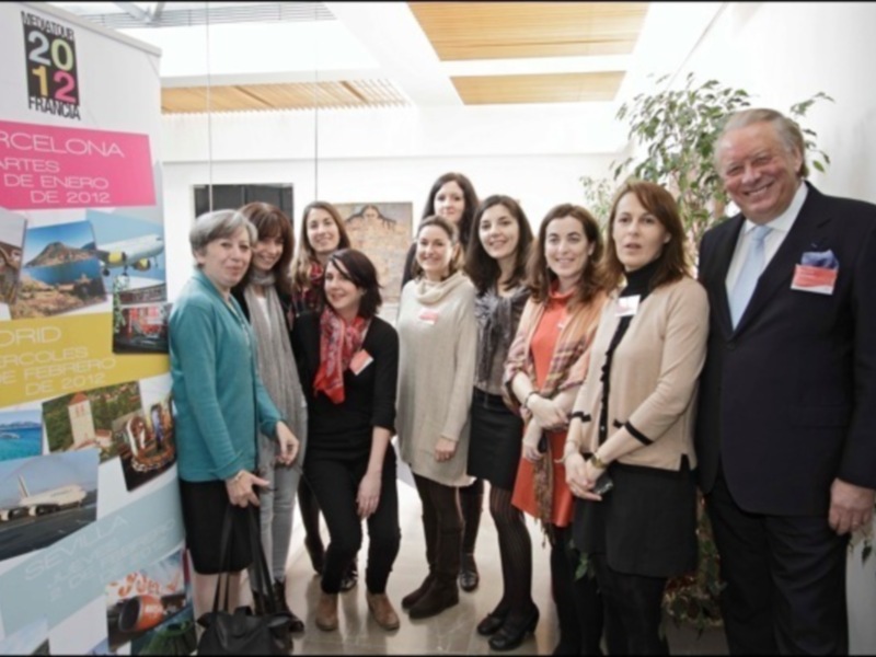 Una foto de grupo de personas en un evento, posando frente a una pared con carteles de viajes.