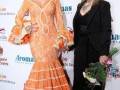 Dos mujeres en un evento de moda, una con un vestido naranja y la otra con un traje negro.