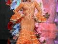 Modelos desfilan en la Semana de la Moda de Sevilla, presentando diseños de trajes de flamenca con detalles en color naranja y azul.