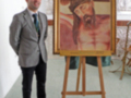 Un hombre en traje posa junto a una pintura de Cristo en una exposición de arte religioso.