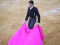 Un torero en acción, con un traje negro y una capa rosa brillante.