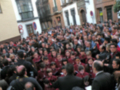 Una multitud en un evento público, posiblemente una manifestación o celebración, con personas vestidas de rojo y negro. El entorno muestra edificios tradicionales, lo que sugiere un lugar histórico o urbano.