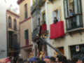 Una procesión religiosa en una ciudad española con gente participando y un hombre en el balcón de una casa mirando la procesión.