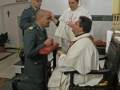 Un sacerdote realiza una bendición en una iglesia, mientras un militar y otro sacerdote observan.