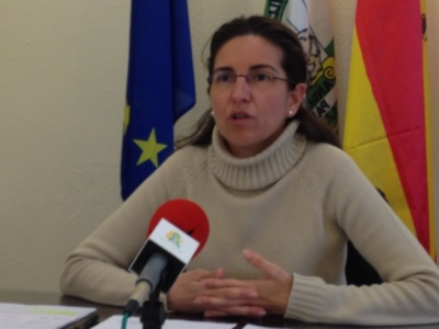 Mujer hablando en rueda de prensa con banderas de la UE y España al fondo.