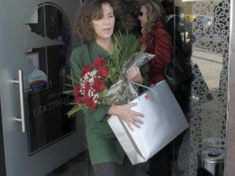 Una mujer con un ramo de flores rojas y una bolsa blanca sale de un edificio.