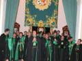Un grupo de personas vestidas con trajes ceremoniales, posiblemente una banda o coro, se encuentra en un entorno decorado con cortinas y un escudo real. La imagen sugiere una celebración o ceremonia formal, posiblemente religiosa o institucional.