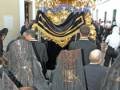 Una procesión religiosa con una carroza dorada y decorada, rodeada de personas vestidas con mantos negros.