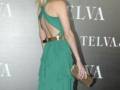 Una mujer con un vestido verde de corte abierto y una cintura dorada, posando en un evento con el logo de Sevillva y Telva al fondo.