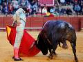 Un torero con capa y muleta enfrentándose a un toro en una plaza de toros.