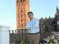 Un hombre en una terraza con flores, frente a la Giralda de Sevilla.
