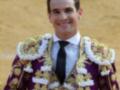 Un torero sonriente en un ambiente festivo, vestido con un traje tradicional de color morado y dorado.