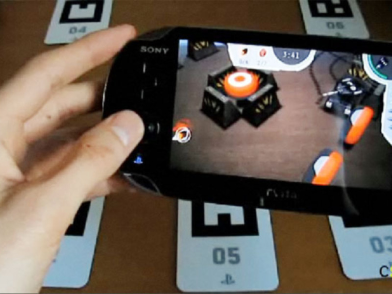 Un juego en un teléfono móvil, con una mano sosteniendo el dispositivo y una pantalla que muestra una escena de juego en 3D. La imagen también incluye algunas tarjetas de cartas al fondo, sugiriendo que podría ser un juego de cartas.