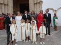 Una familia formada por adultos y niños, todos vestidos formalmente. La imagen muestra una escena de un evento importante en una iglesia o edificio histórico, con gente vestida con trajes y vestidos de gala.