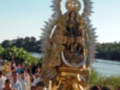 Imagen de una Virgen María en procesión, rodeada de flores y gente.