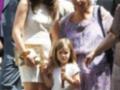Una mujer joven con vestido blanco y gafas de sol, una anciana con vestido púrpura y una niña pequeña en un vestido blanco.