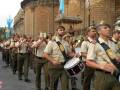 Desfile militar con banda de música y uniformes tradicionales, frente a un edificio histórico.