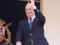El rey Juan Carlos saludando desde un balcón, con el escudo real en el fondo.
