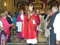 Una imagen de una ceremonia religiosa en un templo, con personas vestidas formalmente y sosteniendo objetos de ceremonia.