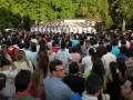 Una multitud de personas asiste a un evento en un parque con árboles verdes en el fondo.