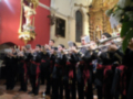 Un grupo de músicos militares toca instrumentos en una iglesia, con un altar y estatuas religiosas al fondo.