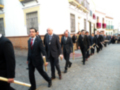 Un grupo de hombres en trajes caminando en fila con palos en las manos, probablemente en una procesión o ceremonia tradicional.