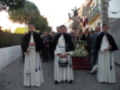 Procesión religiosa con imágenes sagradas y participantes vestidos con trajes tradicionales en una calle urbana.
