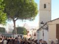 Una multitud se reúne en un entorno urbano, frente a una torre de estilo mediterráneo. La imagen muestra un ambiente festivo o ceremonial, con gente vestida formalmente y árboles verdes alrededor.
