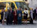 Grupos de mujeres posando frente a un autobús amarillo en una plaza histórica.