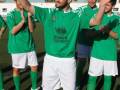 Un grupo de jóvenes vestidos con camisetas verdes y shorts blancos celebrando en un campo de fútbol.