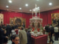 Una exposición de arte religioso con visitantes observando obras de arte enmarcadas y una estructura con una estatua en el centro.