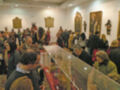 Una sala de exposición con varias personas observando obras de arte en vitrinas. En las paredes, hay cuadros y estatuas que representan figuras históricas. La iluminación es suave, creando un ambiente tranquilo y reflexivo para el público.