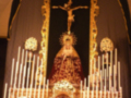 Imagen de una iglesia con un altar principal, la Virgen María en el centro y un crucifijo en el frente. Alrededor del altar hay flores y velas encendidas, creando una atmósfera de reverencia.
