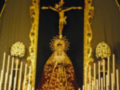 Imagen de una iglesia con un altar dedicado a la Virgen María, rodeada por flores y velas. En el centro, un crucificado se eleva sobre la imagen de la Virgen. La decoración dorada y el altar son destacados, creando un ambiente de reverencia religiosa.