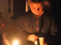 Un niño sostiene una vela en una ceremonia nocturna, iluminando el ambiente con su luz.