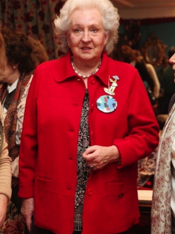 Una mujer con abrigo rojo y insignia, posando en un evento social.
