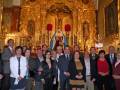 Fotografía de una reunión formal en un ambiente religioso, con personas vestidas formalmente frente a una estatua de la Virgen María en un altar dorado.