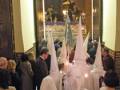 Una procesión religiosa en una iglesia con penitentes vestidos de blanco y sombreros blancos.
