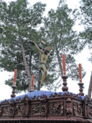 Un crucifijo dorado en un altar de madera con detalles artísticos, rodeado por árboles y una nube en el cielo.