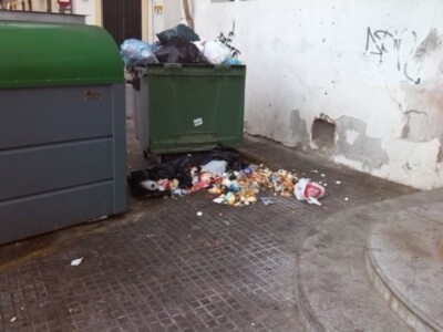 Desechos en el suelo junto a contenedores de basura, evidenciando problemas de limpieza en la calle.