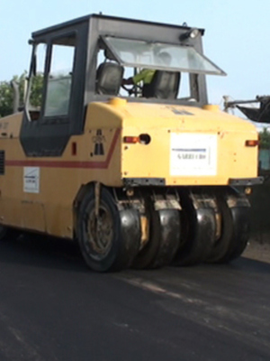 Un vehículo de asfaltado en acción, con un camino recién pavimentado.