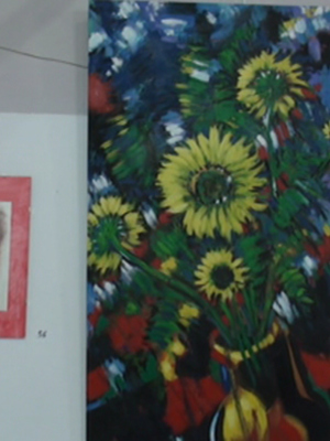 Dos cuadros de arte colgados en una pared. El cuadro izquierdo muestra un retrato en blanco y negro de un personaje con cabello largo, mientras que el cuadro derecho es una pintura vibrante de flores y hojas en colores brillantes.