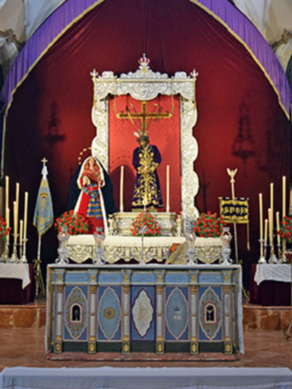 Interior de una iglesia con altar central, estatua religiosa y flores. Ambiente sereno y reverente.