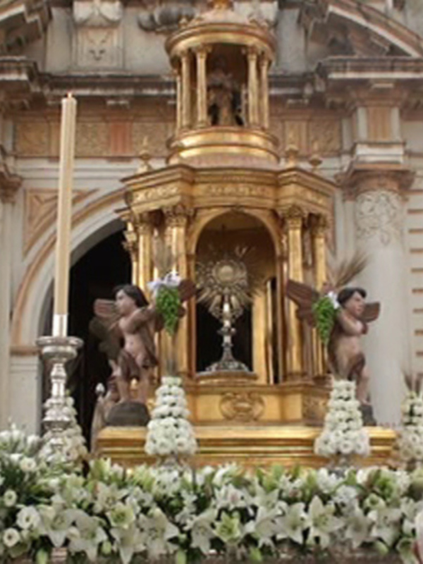 Elegante altar con flores blancas y dorado, adornado con estatuas y velas, frente a una iglesia histórica con detalles arquitectónicos.