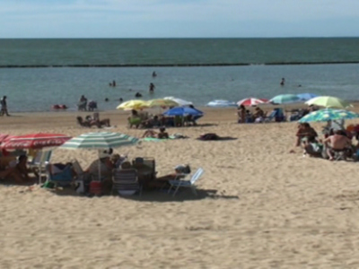 Una hermosa playa con numerosas sombrillas de colores y sillas, donde personas disfrutan del sol y el mar.